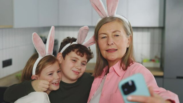 Smiling Grandmother and Grandchildren Doing Selfie Taking a Picture with Easter Eggs, Wearing Bunny Ears, Have Fun Day Together at Home. Happy Easter. Concept of Childhood and Family Weekend