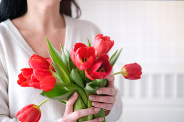 International Womens Day.Close-up of a woman in a white sweater with a bouquet of red tulips