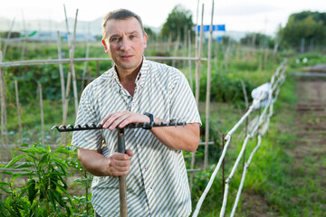 Adult man farmer with rake standing at farm outdoor