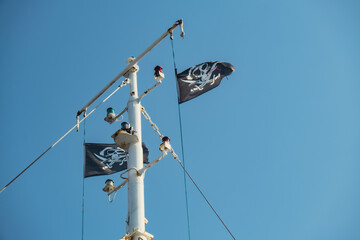 Jolly Roger or pirate ship flag waving with flagpole and blue sky, skull and crossbones, Pirates of...