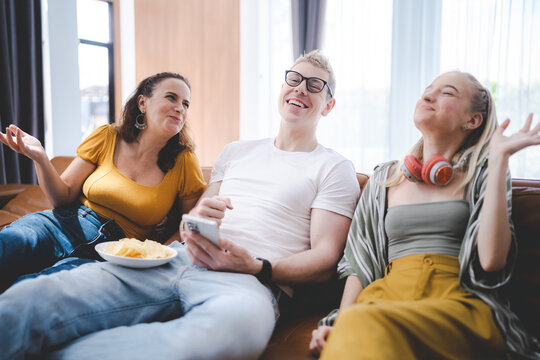 Smiling young family of father with spectacles sitting on couch with wife and daughter wearing headphones around neck at home waving hand on digital tablet screen during online video call
