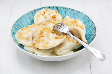 Pierogi or pyrohy or varenyky ( dumplings ) or vareniki stuffed dumplings sprinkled with fried onions and butter with herbs in a plate isolated on a wooden table. Ukrainian or Polish traditional dish.