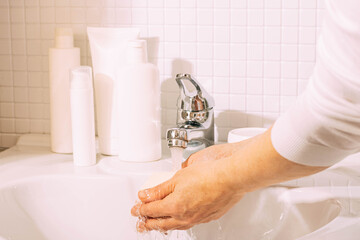 A woman washes her hands under clean running water over a white sink in bathroom. Hygiene and health