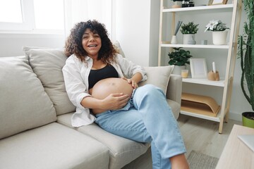 Pregnant woman smile and happiness lies on the couch freedom and strokes her belly with a baby in the last month of pregnancy, mother's day lifestyle