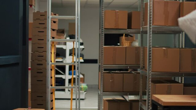 Storage room filled with merchandise packed in boxes, placed on shelves and racks in empty warehouse. Small business space used for shipping products and doing stock inventory.