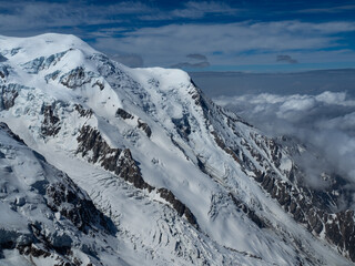 Obraz premium Majestic view of Mont Blanc near Chamonix, showcasing its snow-covered slopes, rugged peaks, and deep crevasses. Clouds hover over the valleys, adding to the breathtaking alpine scenery