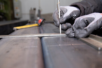 The worker makes a mark on a metal surface. Drilling holes in metal profiles for mounting metal structures. Construction.