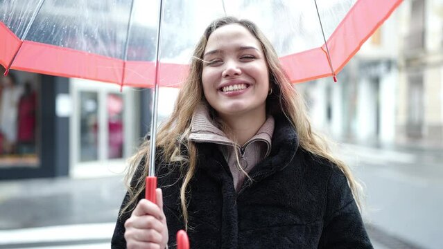 Young beautiful hispanic woman smiling confident holding umbrella at street