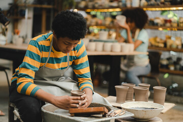 An Afro-haired potter sculpts a ceramic pot from clay on a potter's wheel. Art workshop concept, hands with clay making of a ceramic pot on the pottery wheel, hobby and leisure with pleasure concept
