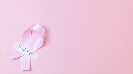 Pink ribbon with sticky tape and the word: hope on a pink background.