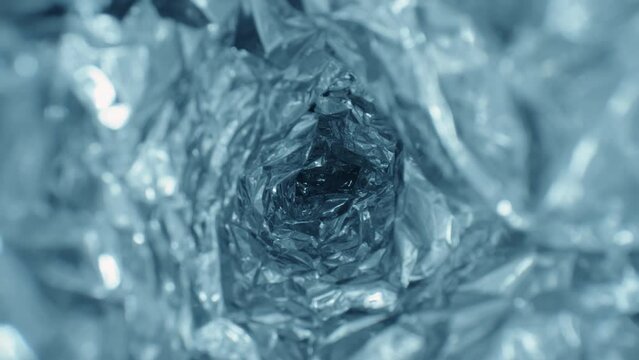 Extreme close-up glide dolly inside shot of blue aluminium foil tunnel ice cave imitation, shiny crumpled metal texture shot with laowa probe lens, mashed metal paper abstract pattern