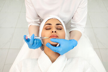 lip augmentation procedure in a cosmetology clinic, cosmetologist doctor makes injection with...