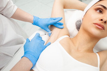 doctor cosmetologist with syringe makes injection of botulinum toxin into the armpit of patient in cosmetology