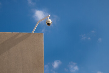 Surveillance camera on top of building with bright blue sky in background and copy space.