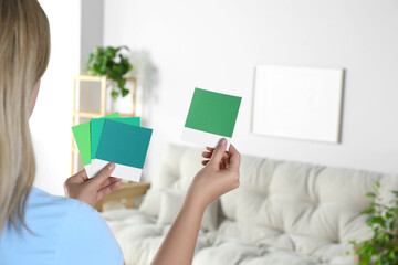 Woman choosing paint shade for wall in room, focus on hands with color sample cards. Interior design