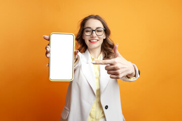 business girl in glasses and suit shows blank smartphone screen on colored background, woman manager advertises phone - obrazy, fototapety, plakaty