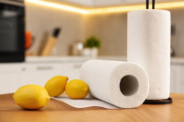 Rolls of white paper towels and lemons on wooden table in kitchen, closeup. Space for text