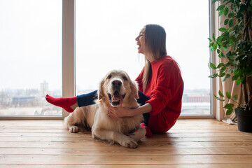 girl plays with a dog breed golden retriever at home on floor, woman with a pet together lies on floor near the window