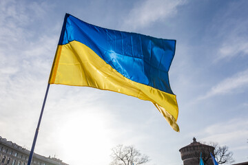 Flag with yellow and blue striped colors of Ukraine waving in the wind with a blue sky and sun.