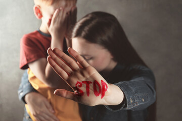 Scared little boy and mother with word Stop written on hand against light grey background, closeup. Domestic violence concept - obrazy, fototapety, plakaty
