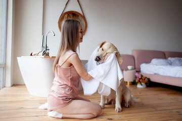 girl in the bathroom wipes her dog with a towel, a woman dries a golden retriever after bathing