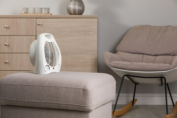 Modern electric fan heater on pouf in cozy room