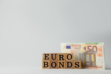 Word Eurobonds made of wooden cubes with letters and banknotes on light grey background. Space for text