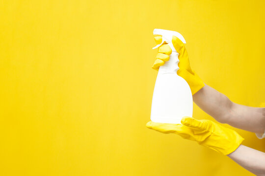 hands in yellow cleaning gloves hold detergent in bottle, empty cleaning spray in the hands of person