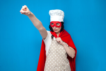 girl chef in superman costume holds kitchen item on blue background, woman housewife in superhero...