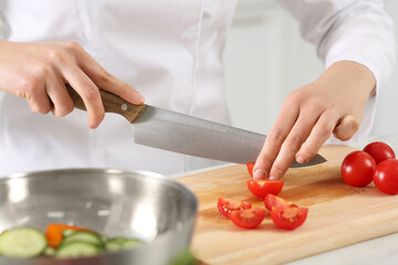 Professional chef cutting fresh tomatoes at white marble table in kitchen, closeup