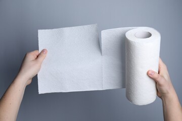 Woman tearing paper towels on grey background, closeup