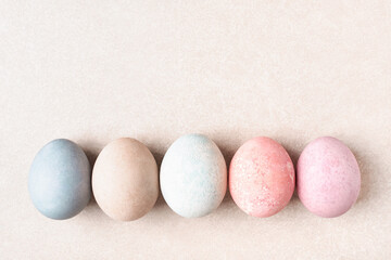Pastel dyed Easter eggs in row on beige background as copy space. Natural pale colors.