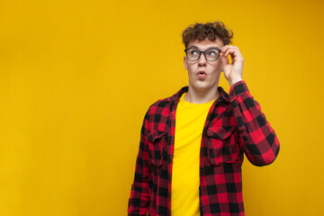 surprised guy student with curly hair holding glasses, cute nerd in glasses on yellow background