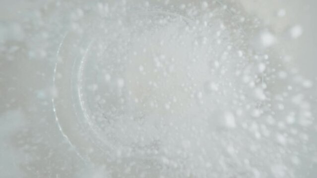 Top down view close-up effervescent tablet in glass of water slow motion shot, white round bubbling aspirin in water, pill dissolves with bubbles