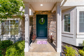 Dark green front door with wreath and purple doormat in between potted plants at the house...