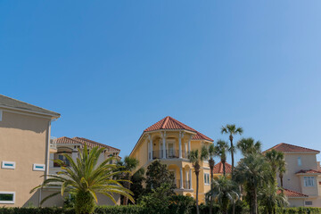 Views of large mediterranean residences behind the vine-covered wall at Destin, Florida. There are trees outside the wall of the houses with tiles roofs against the blue sky background.