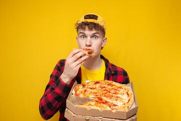 shocked guy eats pizza on yellow background and shows surprise, hungry student enjoys fast food