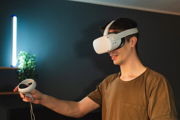 A young guy is wearing virtual reality googles or head set and playing in virtual reality in his...