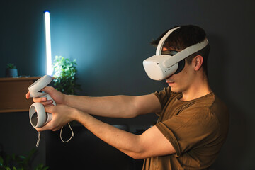 A young guy is wearing virtual reality googles or head set and playing in virtual reality in his room	
