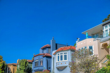Fototapeta na wymiar Facade of colorful multi-storey homes in San Francisco against blue sky. Peaceful residential neighborhood with trees and cloudless sky viewed on a sunny day.