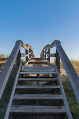 Stairs of a wooden footbridge above the grassy sand dune in Destin, Florida. Wooden walkway over the protected sand dune below with view of clear blue skyline.