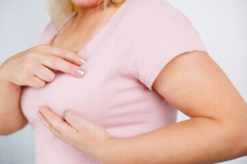 Young woman in pink t-shirt with breast pain touching chest.