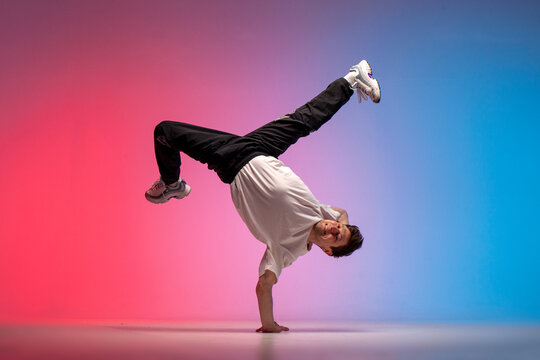 dancer doing acrobatic trick and dancing breakdance in neon red and blue lighting, young energetic guy