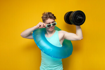 young guy in the summer on vacation with an inflatable swimming circle holds a big heavy dumbbell and goes in for sports