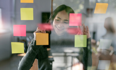 Creative businesswoman writing on sticky notes on a glass wall