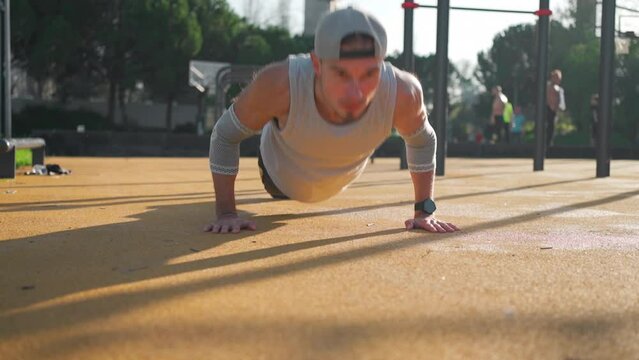 Athletic man doing push up exercises on sports ground in park. Caucasian male athlete doing press up workout training outside gym sunny summer day.