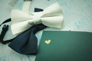 Green bow tie and white bow tie with green notebook with golden heart logo, top view. Flat lay of...