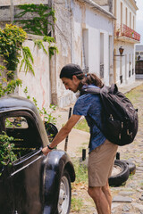 Young latin man trying to open the door of an abandoned car that has been taken over by nature....