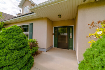 House entrance with wide glass front door with ornate side panels. There are plants at the front of...