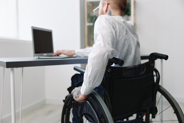 A man wheelchair businessman with tattoos in the office works at a laptop online, business process,...
